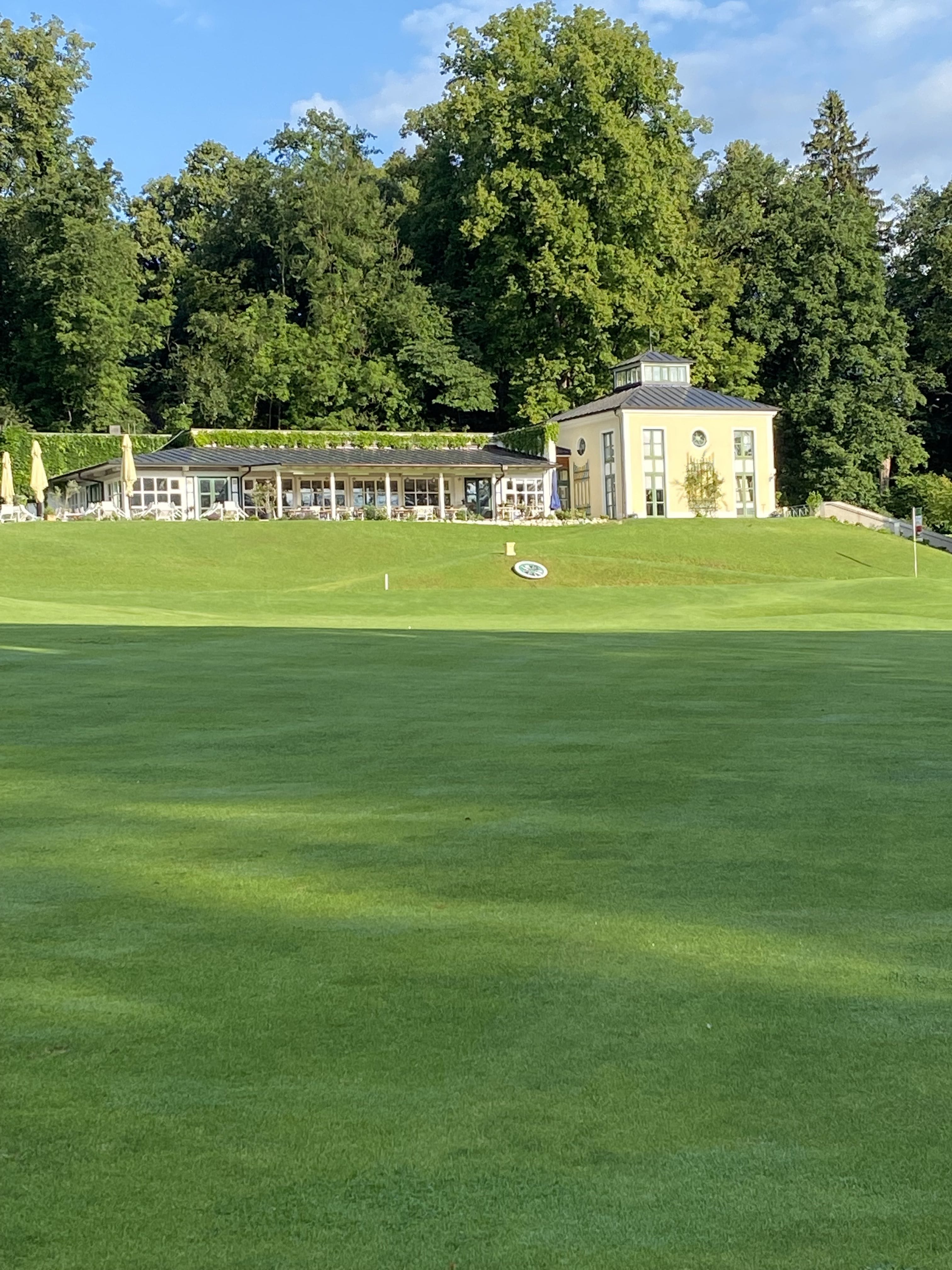 Clubhaus mit Terrasse über dem Fairway, umgeben von alten Bäumen